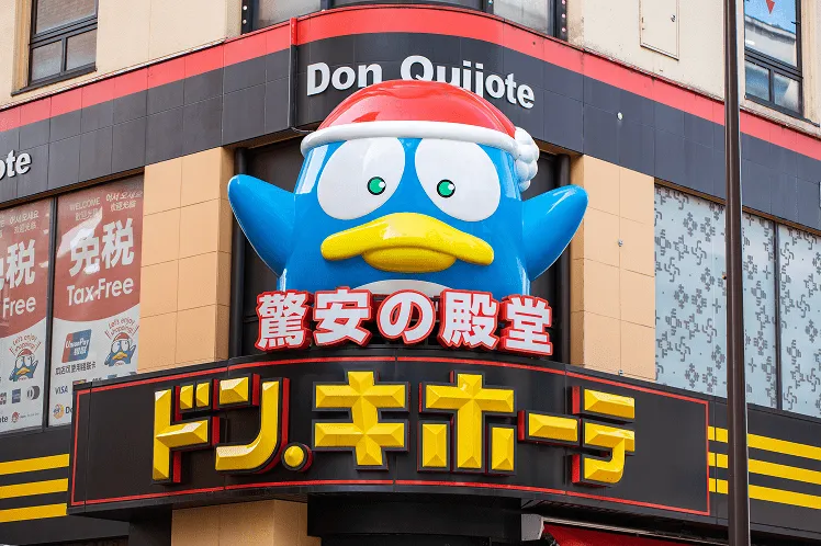 Don Quijote shopping mall entrance featuring a blue penguin mascot wearing a Christmas hat, welcoming visitors with holiday cheer in Japan