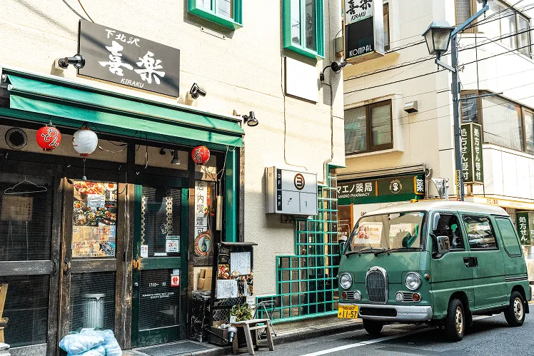 Retro-style green van parked in front of a traditional restaurant decorated with lanterns and menus, capturing the charm of everyday city life
