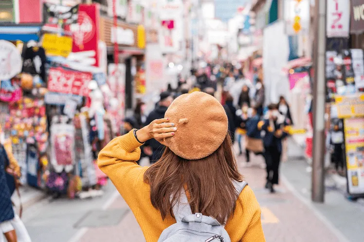 A young girl dressed in vibrant autumn colors of yellow and brown stands amid a lively crowd of youths in Shibuya, capturing the dynamic energy of Tokyo’s bustling urban life