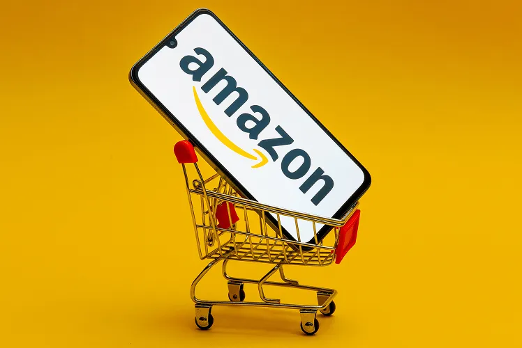 Amazon logo on the smartphone screen in a toy market cart on a yellow background