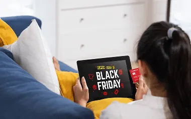 a woman doing online shopping with a credit card on black Friday sale on a tablet sitting on a sofa at home