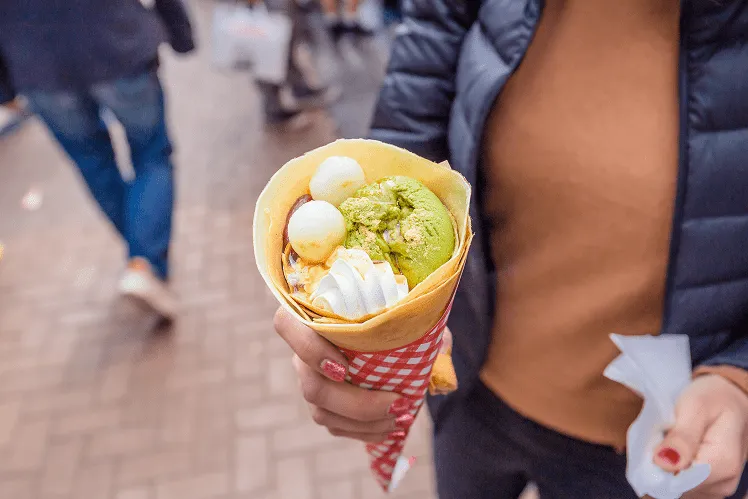 On bustling Takeshita Street, a girl holds a popular Harajuku crepe filled with green tea ice cream, sweet red bean, and fresh cream, folded into a delicate cone