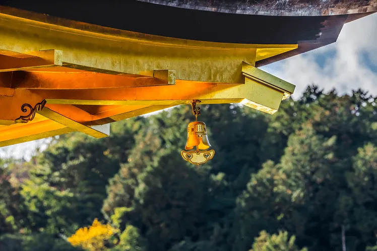 The golden bell hanging at the corner of Kinkaku-ji, a serene Buddhist temple, gently chimes as the soft breeze passes by, filling the air with a soothing melody for visitors to enjoy