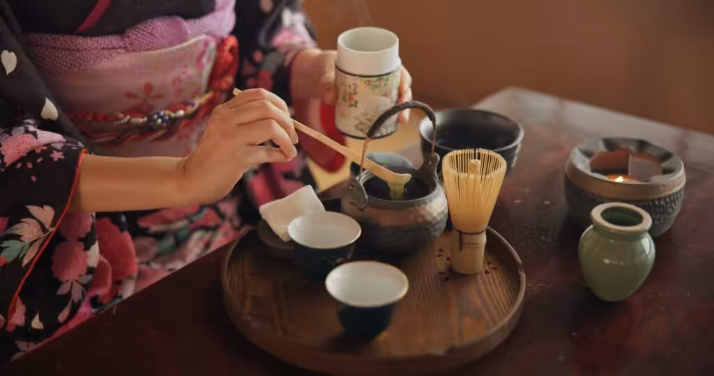 A traditional Japanese woman prepares matcha tea with herbs, powdered tea, and a teapot, embodying the ritual and indigenous cultural wellness practices with a focus on craftsmanship and mindfulness