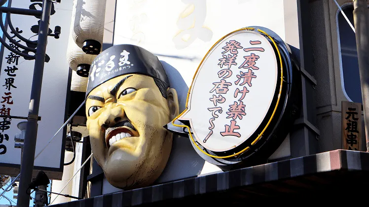 The iconic Kushikatsu Daruma restaurant façade in Osaka’s bustling Dotonbori district, featuring the famous 'angry chef' face sculpture above the entrance